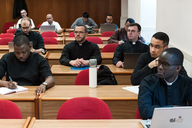 Jaunie katoļu semināristi un priesteri apmeklē nodarbības universitātes auditorijā, tērpušies melnos sutanās vai garīdznieku kreklos ar apkaklēm. Viņi ir uzmanīgi, pierakstot piezīmes vai izmantojot klēpjdatorus, kas ir daļa no viņu intelektuālās un garīgās formācijas, lai pilnībā izdzīvotu savu aicinājumu un apņemšanos ievērot priesterības celibātu.
