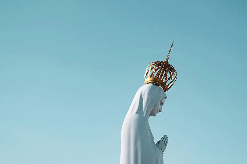 Estatua de la Virgen María con corona dorada sobre un fondo azul claro, simbolizando su realeza.