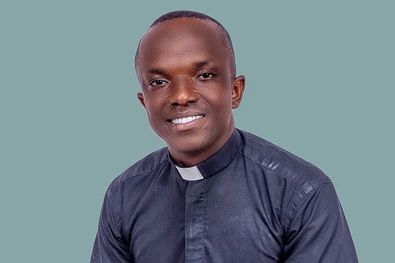 Sacerdote nigeriano Emmanuel Enwenwen, beneficiario de la Fundación CARF, con hábito clerical, mirando al frente y sonriendo.