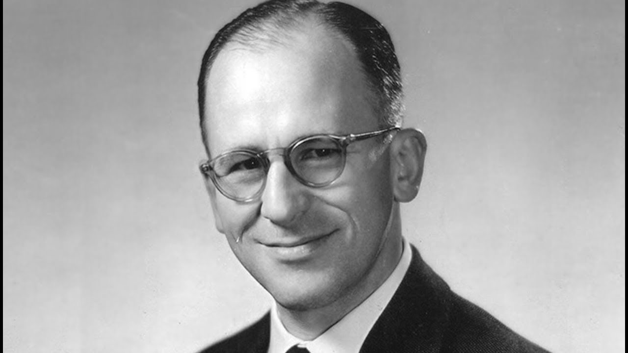 Retrato en blanco y negro de Enrique Shaw, con gafas y traje, sonriendo ligeramente.